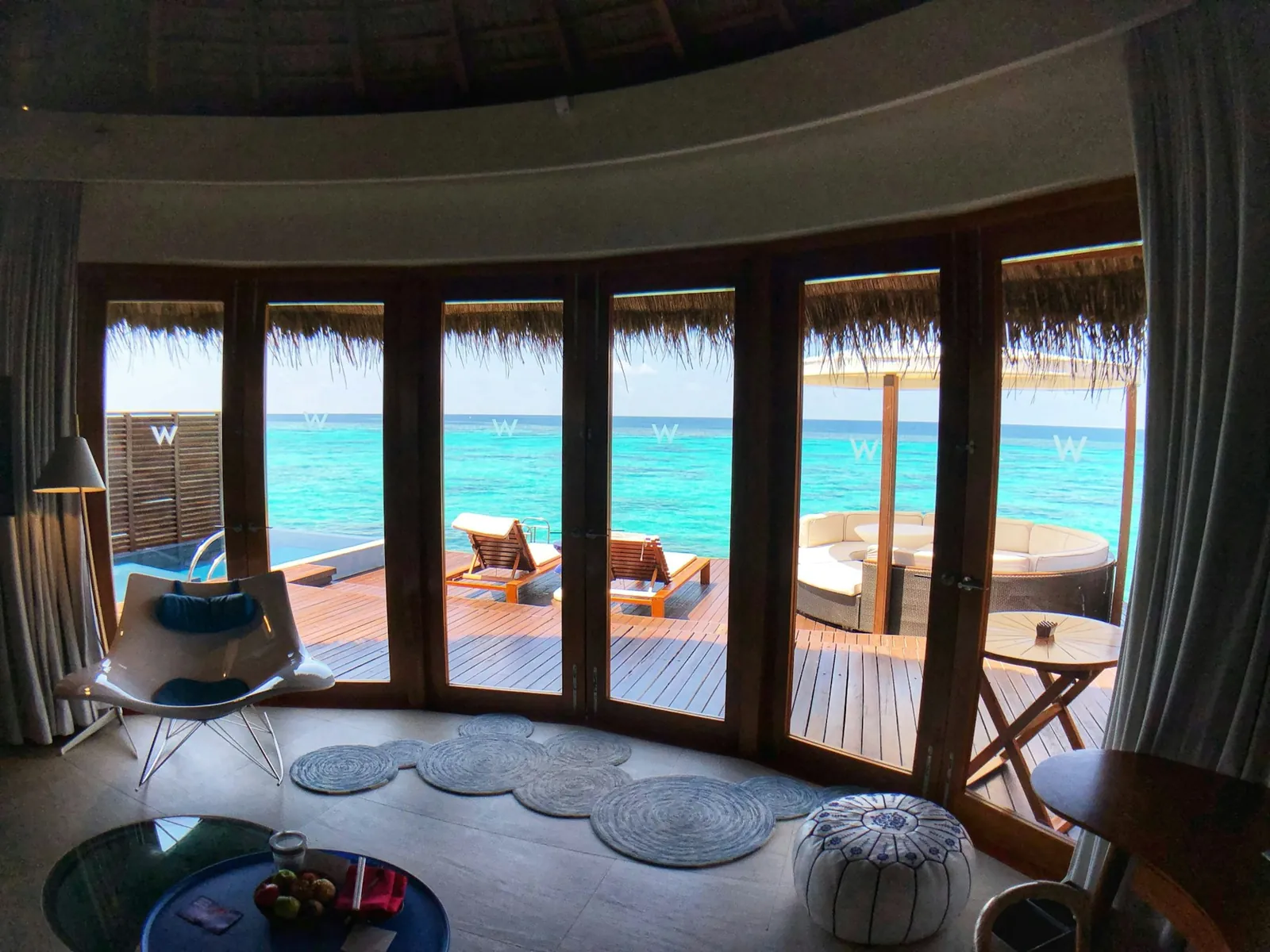 Wohnbereich einer privaten Overwater-Villa mit Panoramafenstern, Sonnendeck und Blick auf die türkise Lagune – Honeymoon-Unterkunft für Flitterwochen