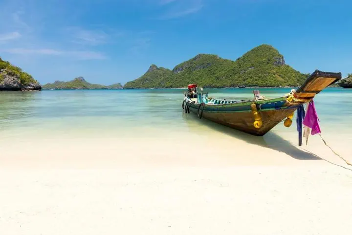Longtailboot vor Kalksteinfelsen und türkisfarbenem Wasser in der Andamanensee in Thailand – Inselzeit in Asien