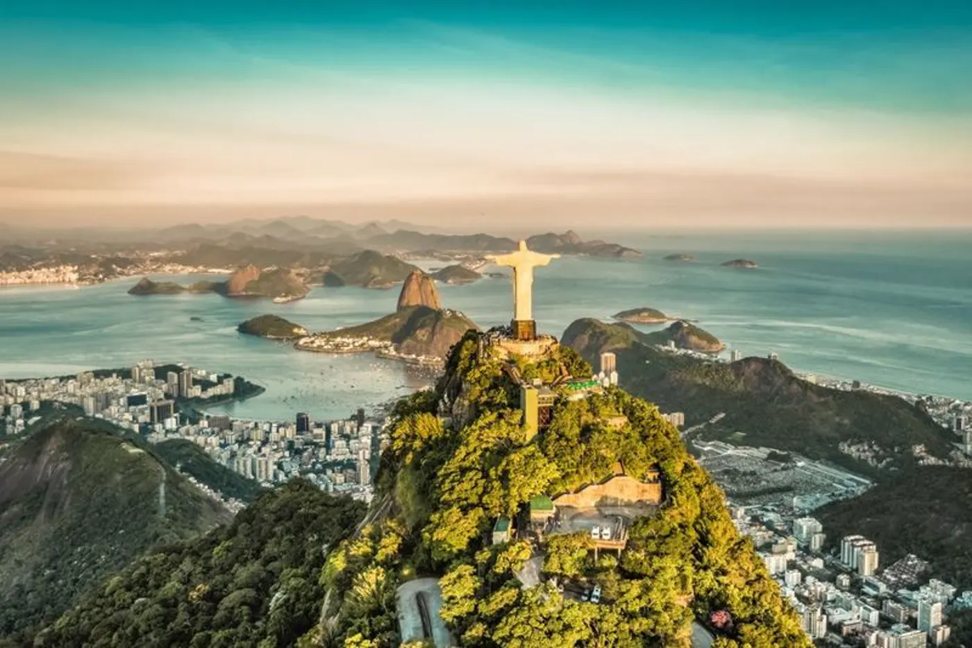 Christusstatue auf dem Corcovado über der Guanabara-Bucht und dem Zuckerhut in Rio de Janeiro, Brasilien, im goldenen Abendlicht