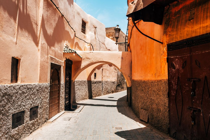 Sonnendurchflutete Gasse in der Medina von Marrakesch mit ockerfarbenen Lehmmauern und geschnitzter Holztür — Luxusreise Marokko Sonnendurchflutete Gasse in der Medina von Marrakesch mit ockerfarbenen Lehmmauern und geschnitzter Holztür — Luxusreise Marokko