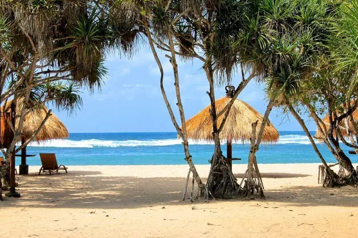 Palmenbeschatteter Sandstrand mit Sonnenliege in Nusa Dua auf Bali, Indonesien Palmenbeschatteter Sandstrand mit Sonnenliege in Nusa Dua auf Bali, Indonesien